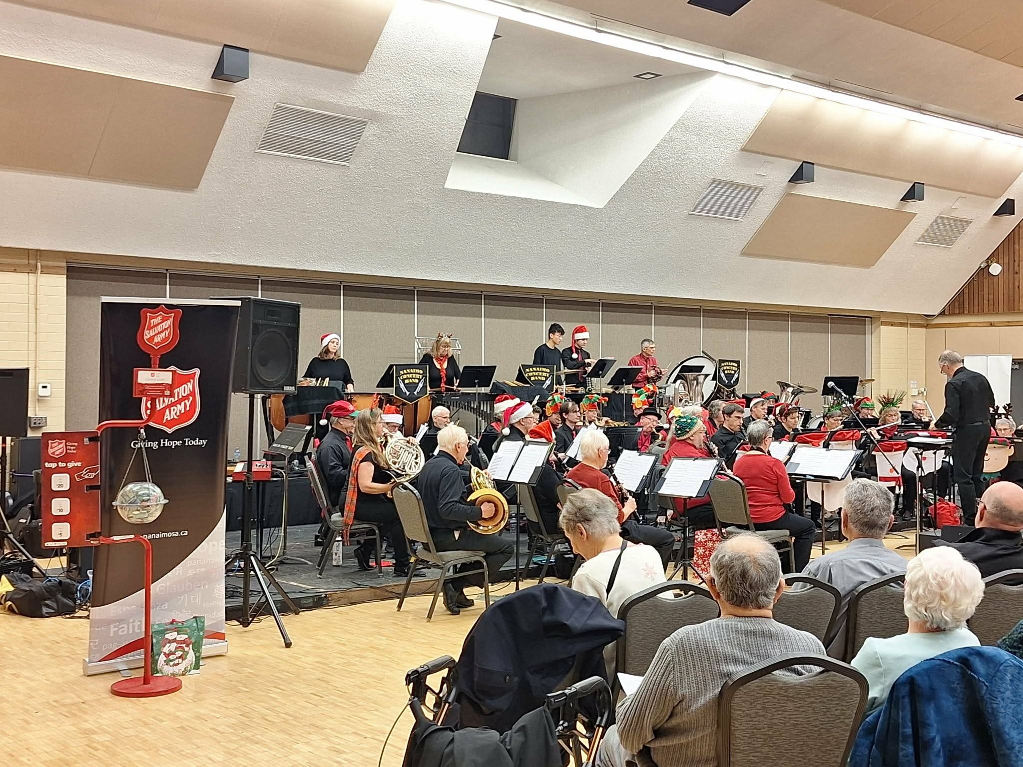 Salvation Army concert band performing on stage in an auditorium, with seated audience members in the foreground.