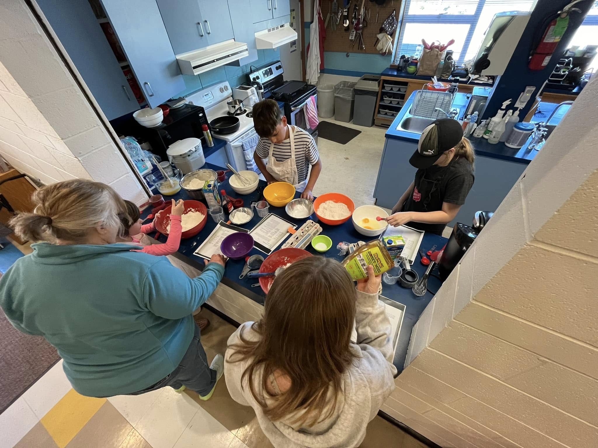 Children and adults preparing food together in a kitchen as part of a kids’ cooking program.