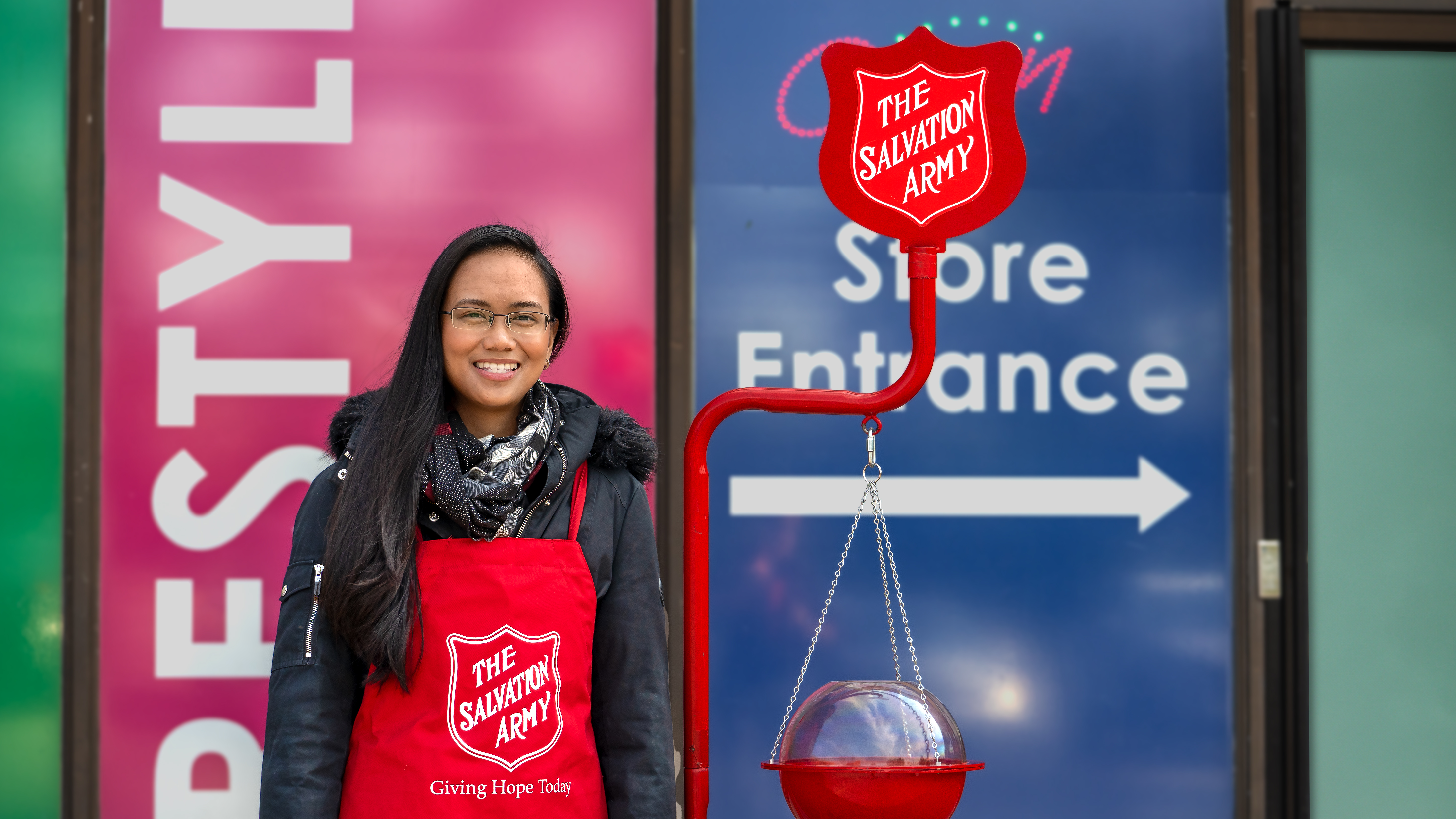The Salvation Army volunteer in a red apron standing next to a red kettle during the Christmas Kettle Campaign.