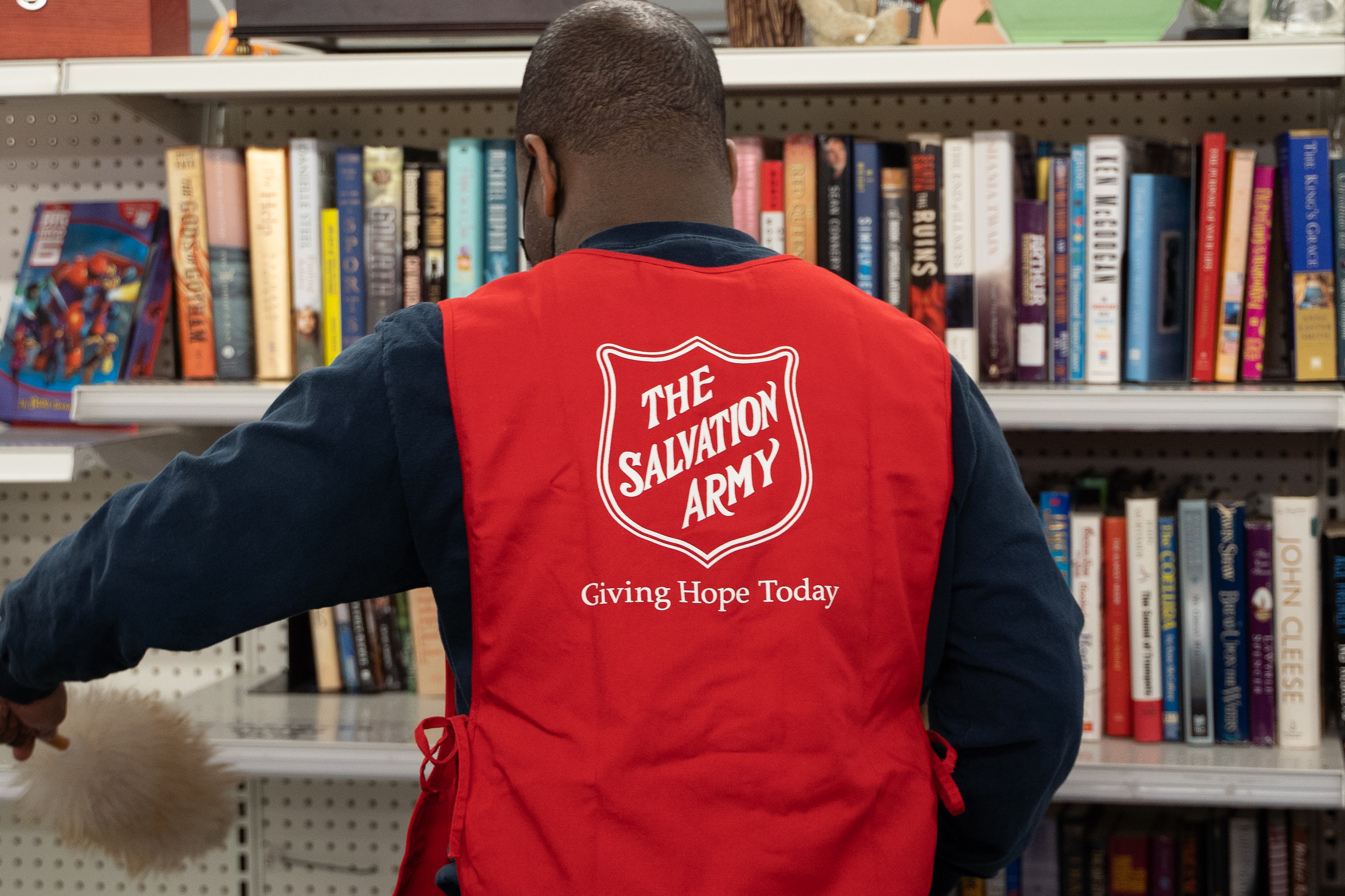 Volunteer wearing a red Salvation Army vest organizing books on shelves.