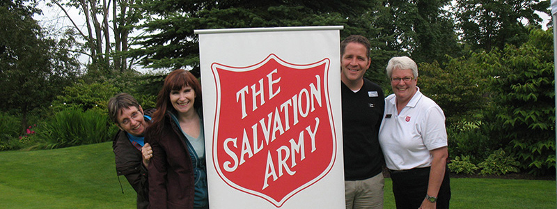 Group of the Salvation Army staff and supporters standing outdoors beside a red Salvation Army shield sign.