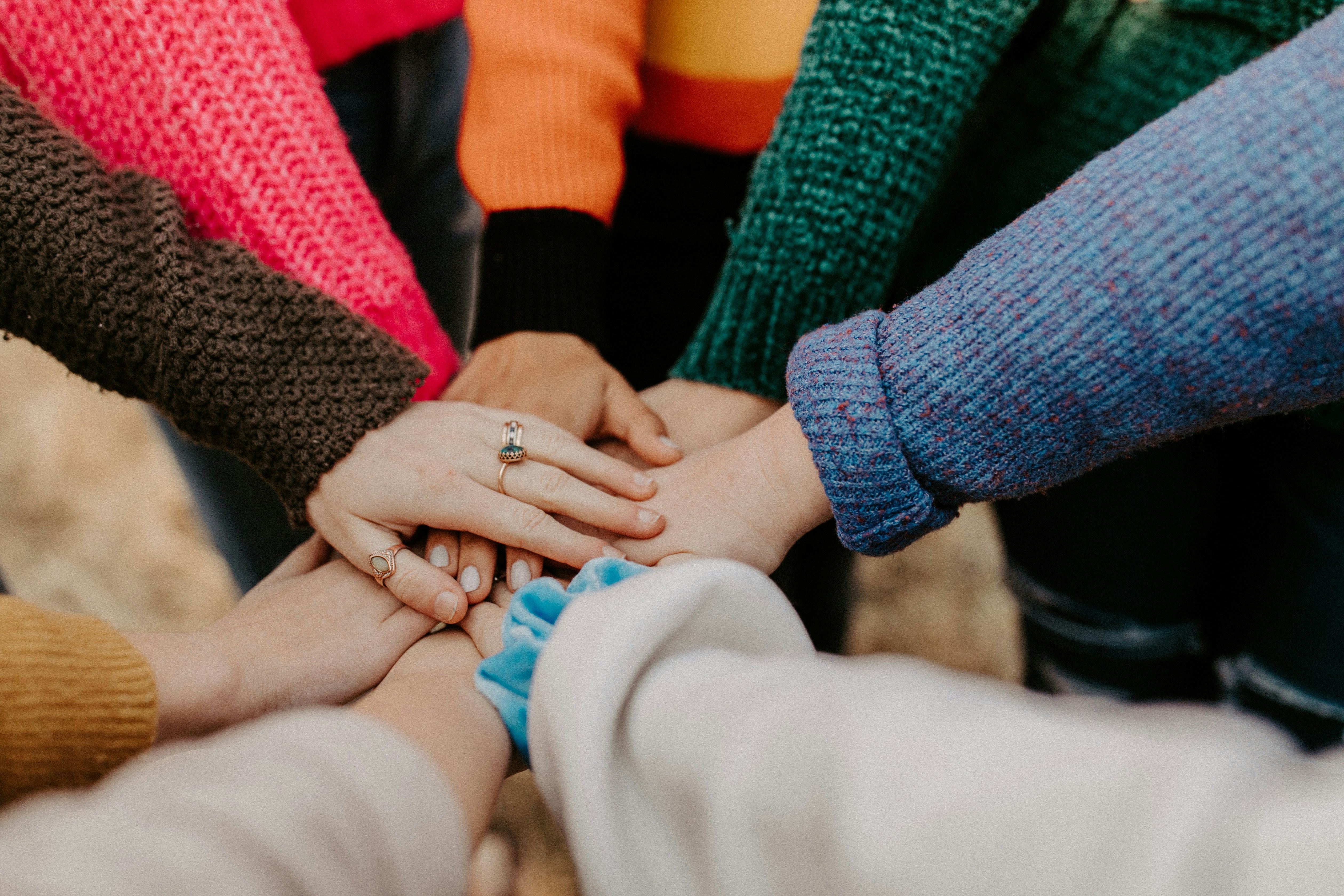 Close-up of several people standing together with their hands stacked in the center, symbolizing support, connection, and community.