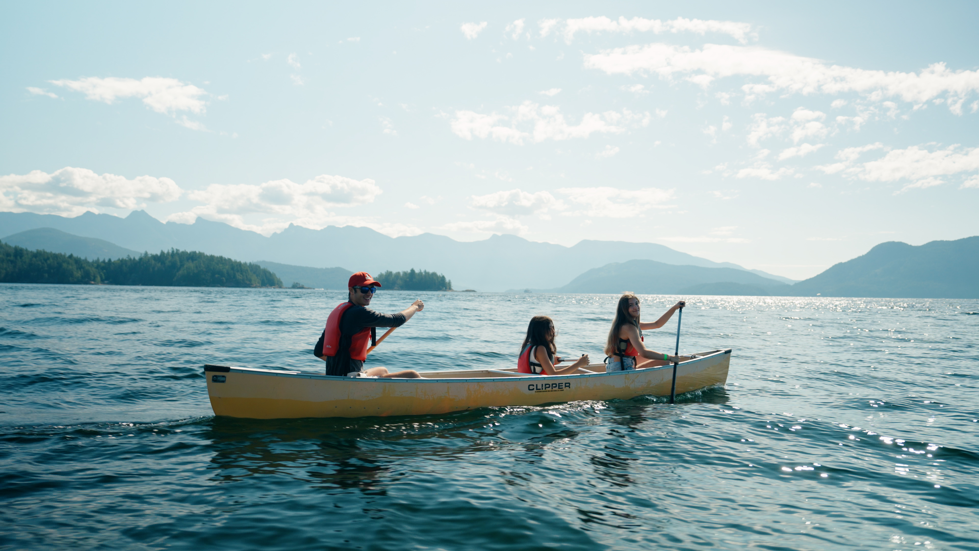 Children canoeing on a lake during a summer camp experience, with mountains in the background.